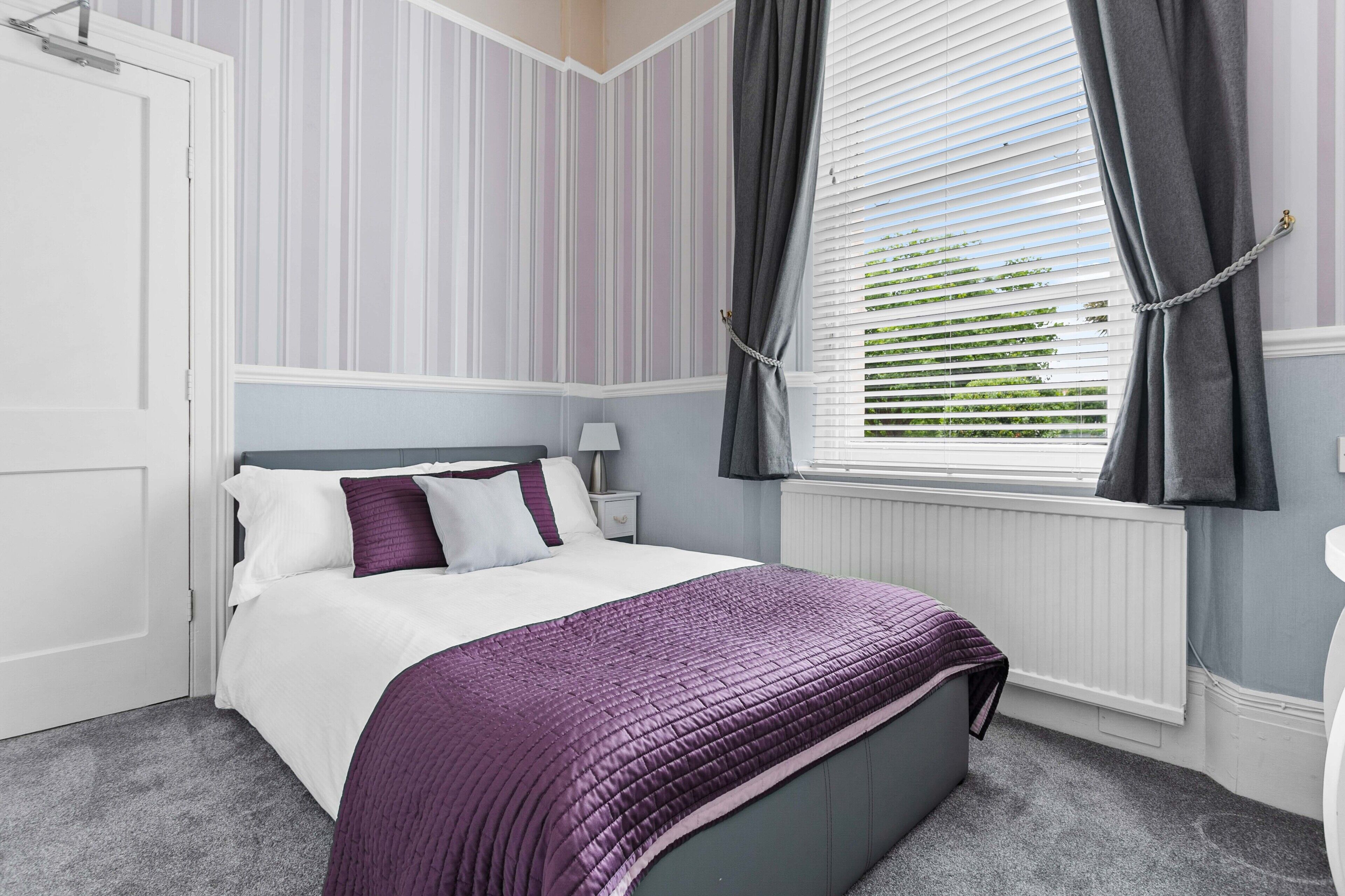Een slaapkamer met een bed, een nachtkastje, een raam met gordijnen en een radiator.