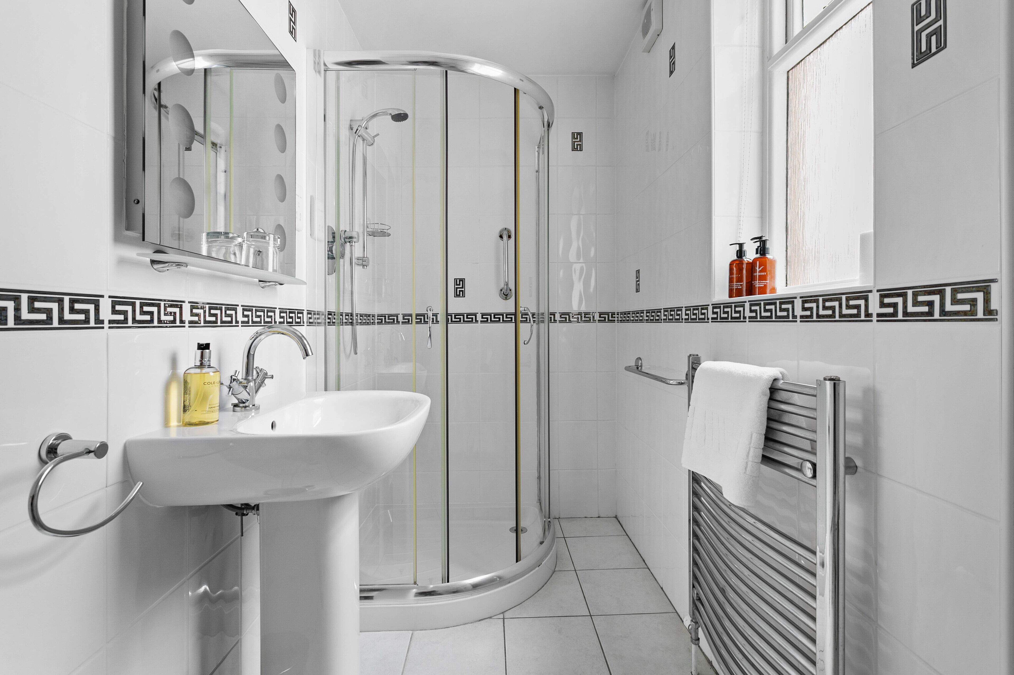 Un baño moderno con cabina de ducha de vidrio, un lavamanos con espejo y un perchero para toallas.