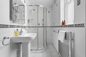 A modern bathroom with a glass shower enclosure, a sink with a mirror, and a towel rack. - The Berburry (Torquay)