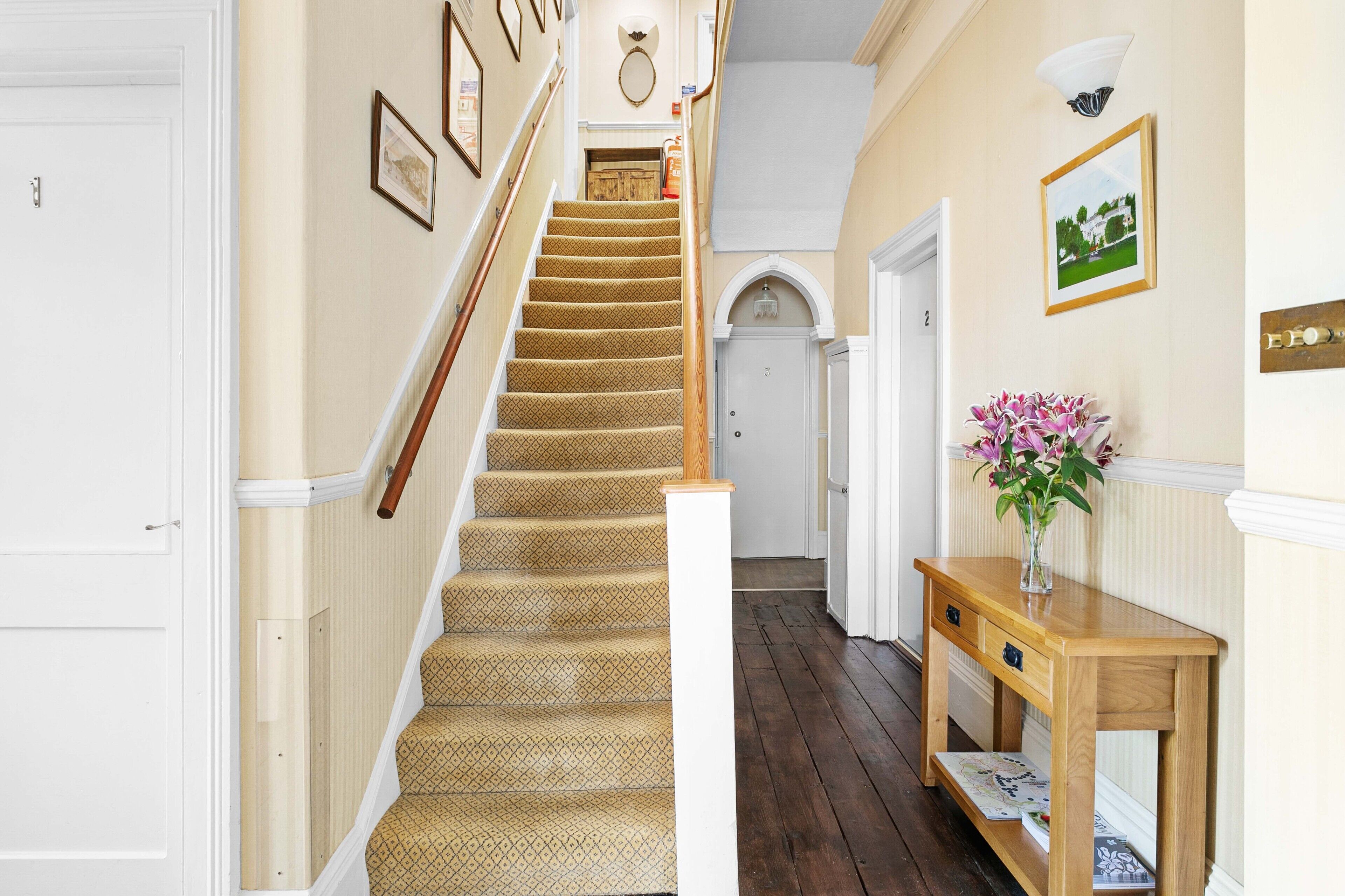 A staircase with patterned carpet, a wooden handrail, and a white door at the top.