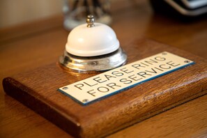 A wooden reception desk with a sign that reads "PLEASE RING FOR SERVICE." - The Berburry (Torquay)