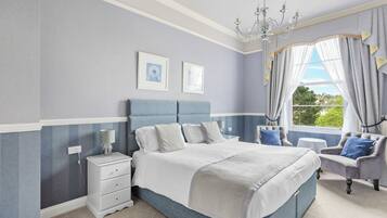 Une chambre à coucher avec un grand lit, une table de chevet, une chaise, un lustre et une fenêtre avec des rideaux.