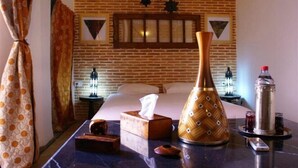 Habitación de hotel con pared de ladrillo, una cama, una mesita de noche con una caja de pañuelos, un jarrón decorativo, una botella y un control remoto.