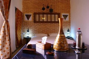 Habitación de hotel con pared de ladrillo, una cama, una mesita de noche con una caja de pañuelos, un jarrón decorativo, una botella y un control remoto.