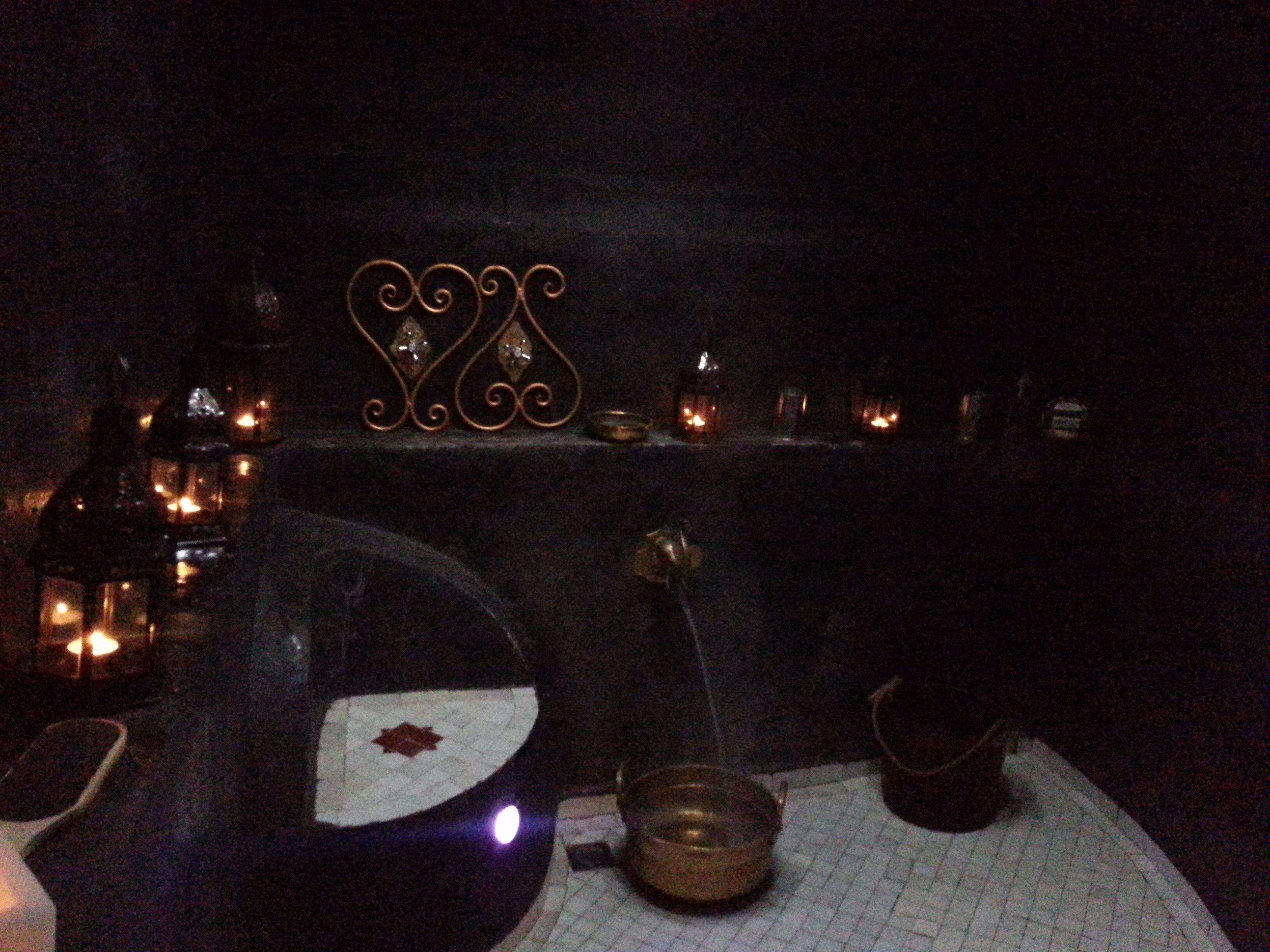 A dimly lit room with a decorative metal sign, a small table with candles, and a few bottles.