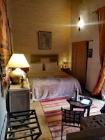 Un dormitorio con cama, mesita de noche, lámpara, silla y una pequeña mesa.