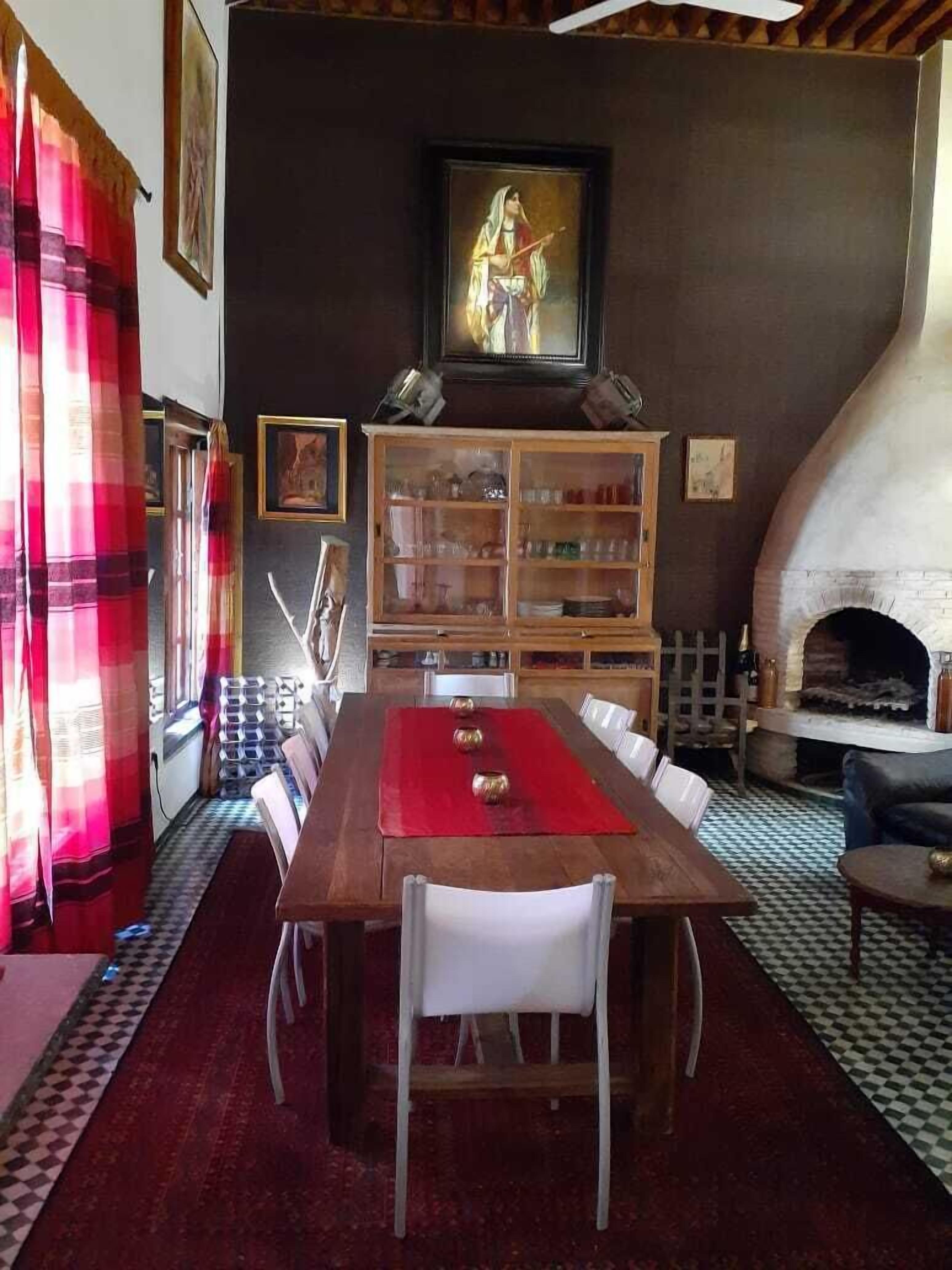 A dining area with a wooden table, white chairs, a red table runner, and a fireplace.
