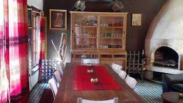 A dining area with a wooden table, white chairs, a red table runner, and a fireplace.