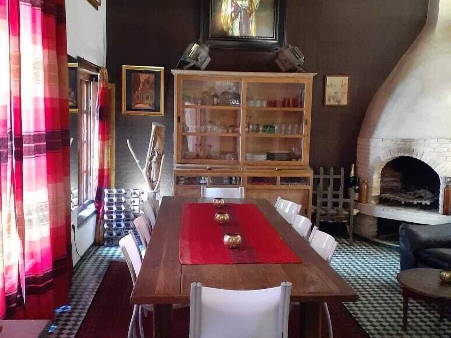 A dining area with a wooden table, white chairs, a red table runner, and a fireplace.