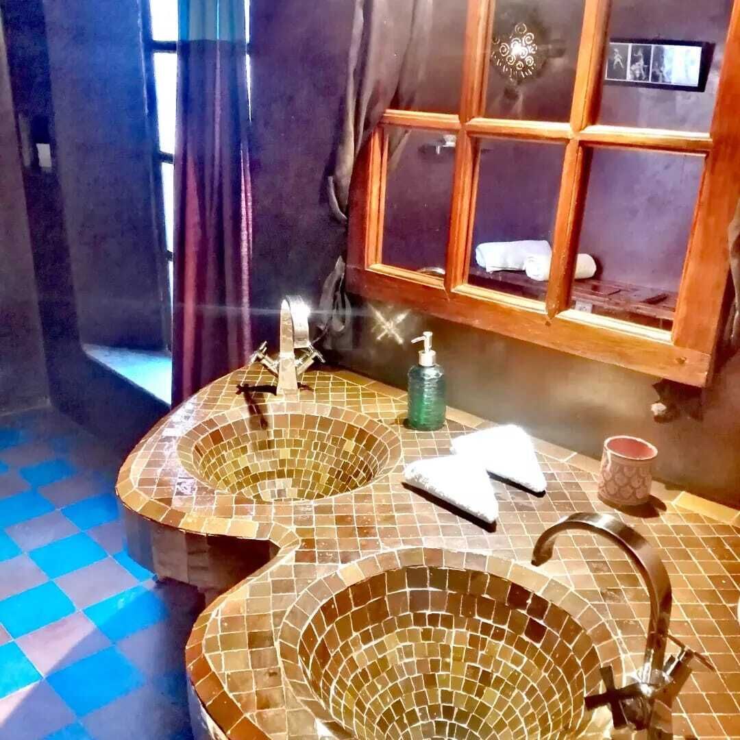 Un baño con dos lavamanos de mosaico, una ventana con vistas, y un suelo azul a cuadros.