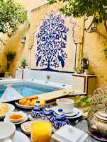 Desayuno junto a la piscina con una pared decorada con azulejos, una piscina pequeña y diversos alimentos para el desayuno.