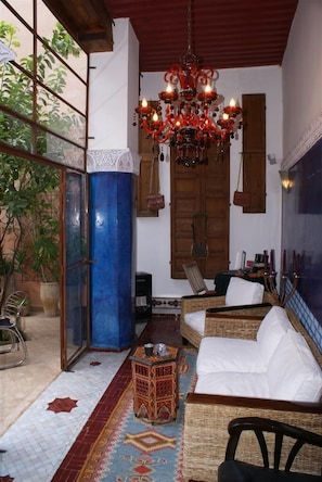 A cozy living room with wicker furniture, a chandelier, and a view through large windows. - Riad Tara (Fes)