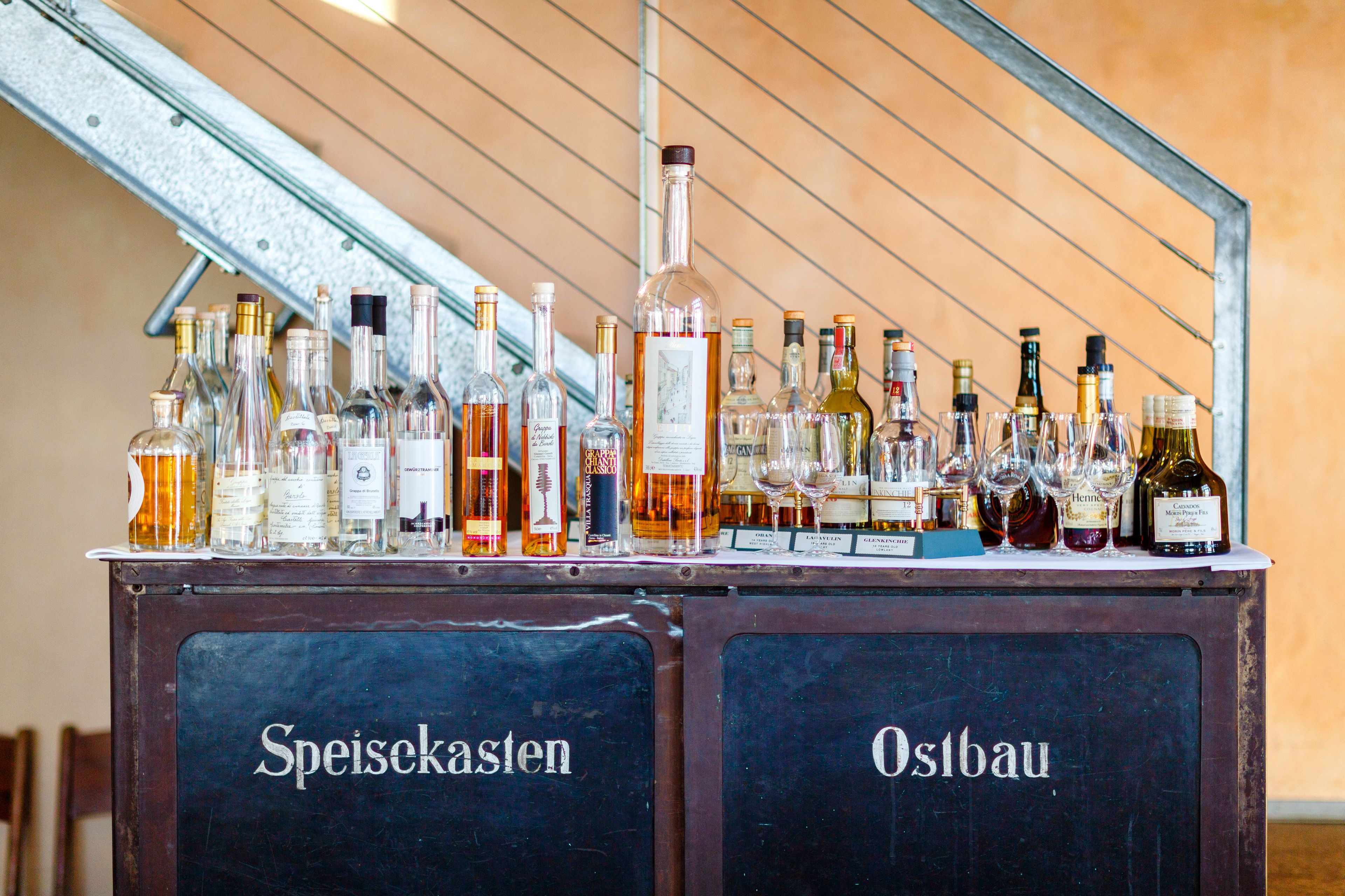 A bar area with a variety of bottles and glasses, labeled with names like "Speisekasten" and "Ostbau".