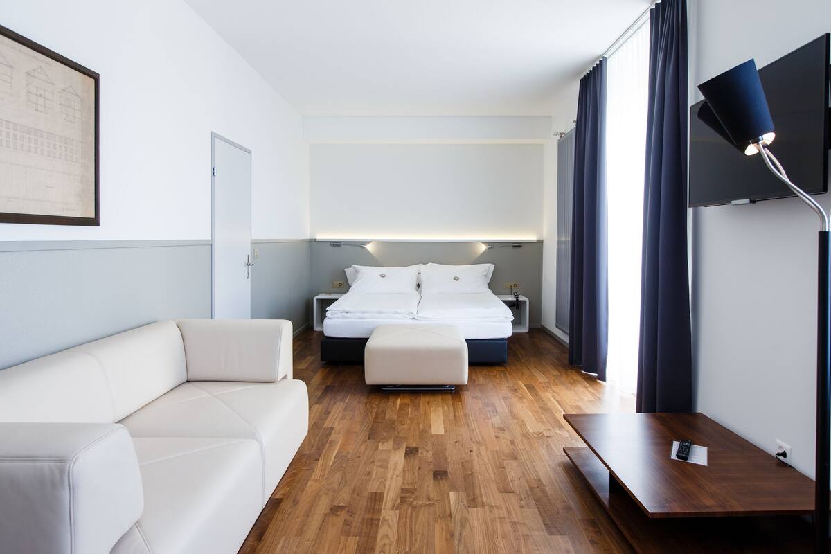 A modern hotel room with a bed, a sofa, a desk, and a TV.