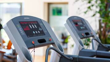 Zwei Trainingsgeräte mit digitalen Anzeigen in einem Raum, auf dessen Schild „Therapie“ steht.