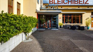 The entrance of Bleichbeiz Hotel with a modern design, featuring a glass door entrance and outdoor seating area.