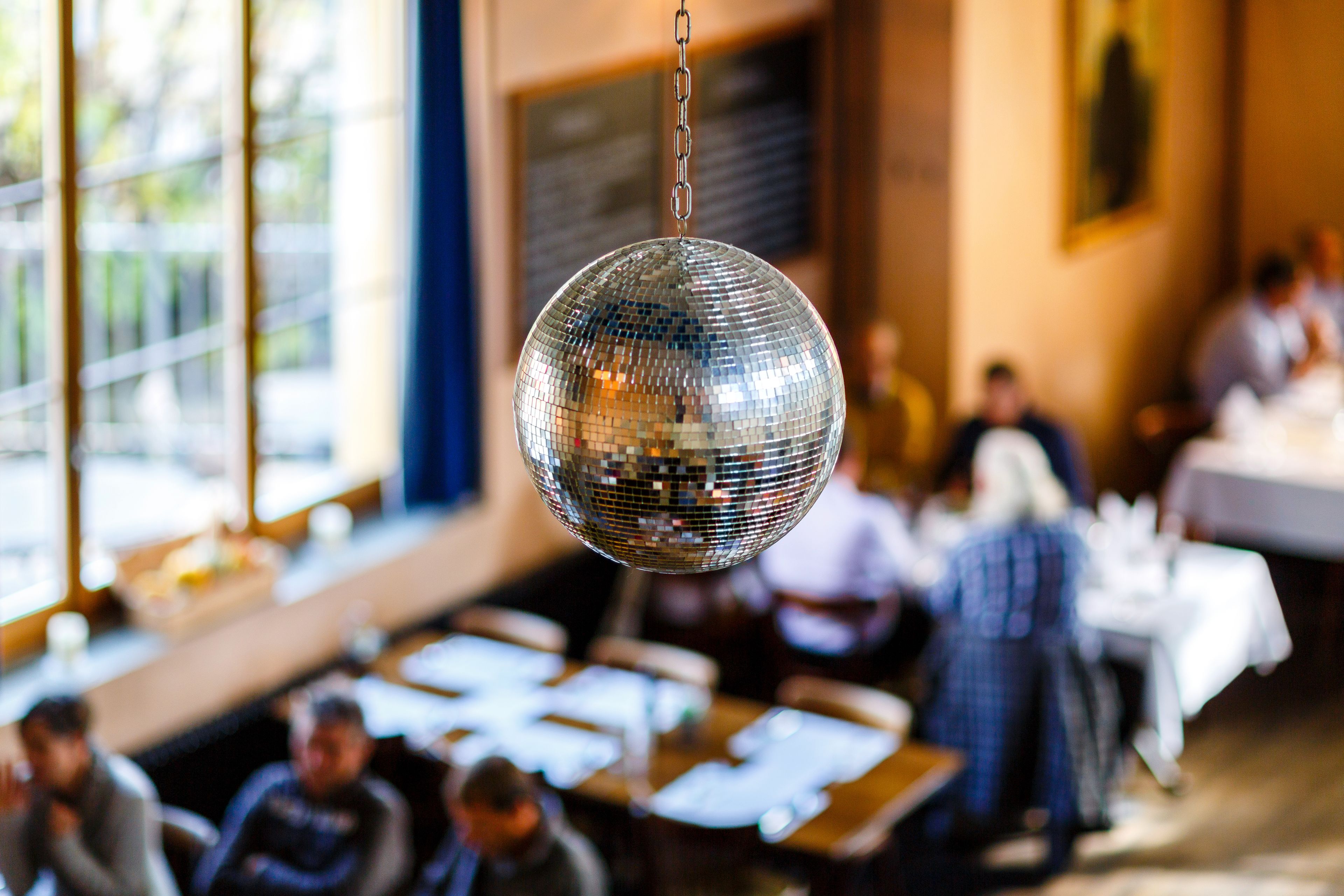 Una bola de discoteca colgando en una sala con mesas y sillas, sugiriendo un espacio para comer o socializar.