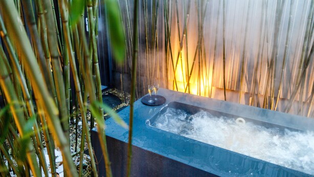 A hot tub with two glasses of wine, surrounded by bamboo plants.