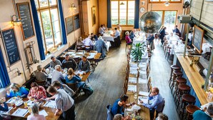 A spacious restaurant with high ceilings and large windows, featuring multiple dining areas and a variety of seating options.