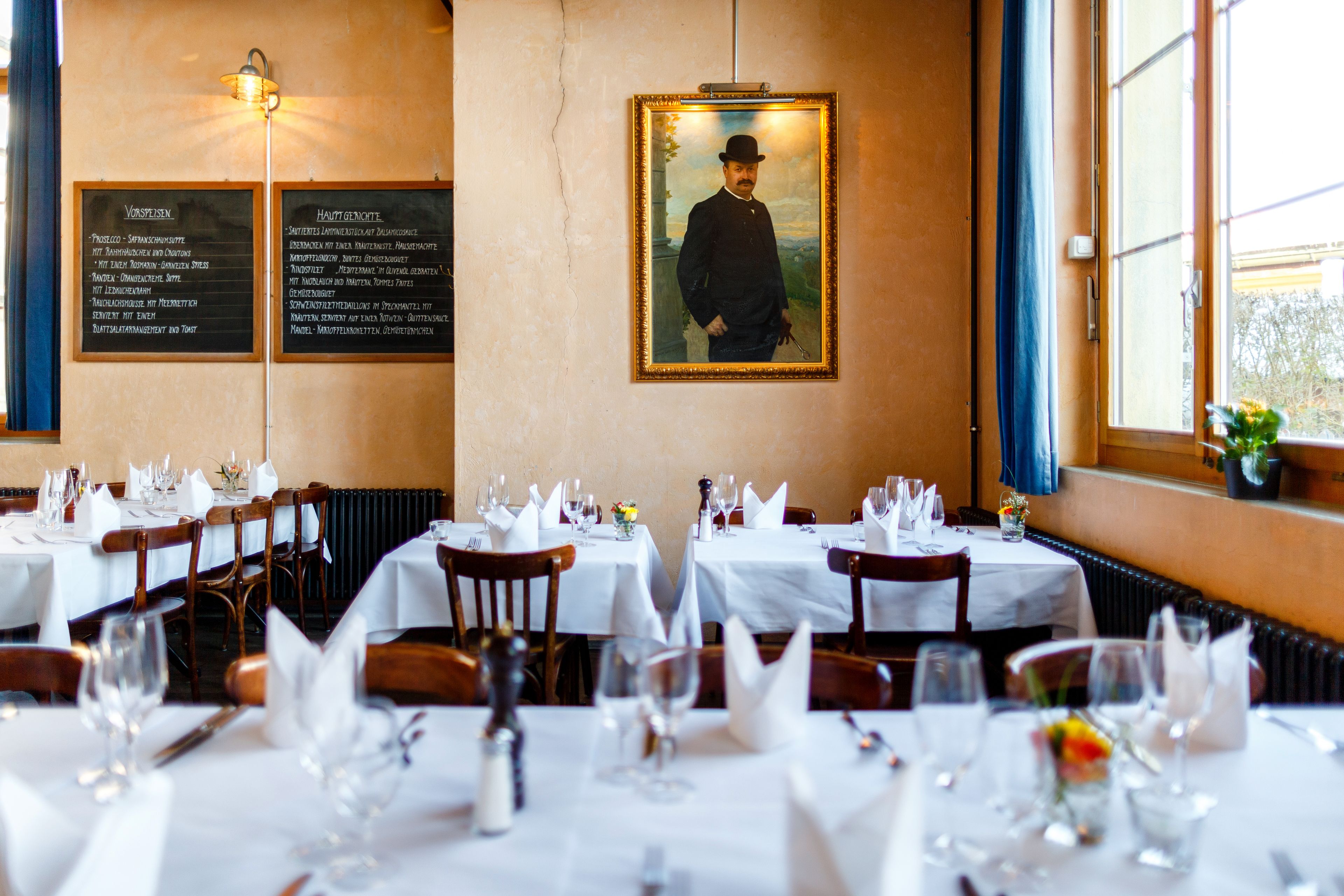 Un restaurante con mesas dispuestas para comer, un retrato enmarcado en la pared y carteleras con el menú.
