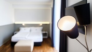 A modern hotel room with a neatly made bed, a bedside table, and a wall-mounted lamp.
