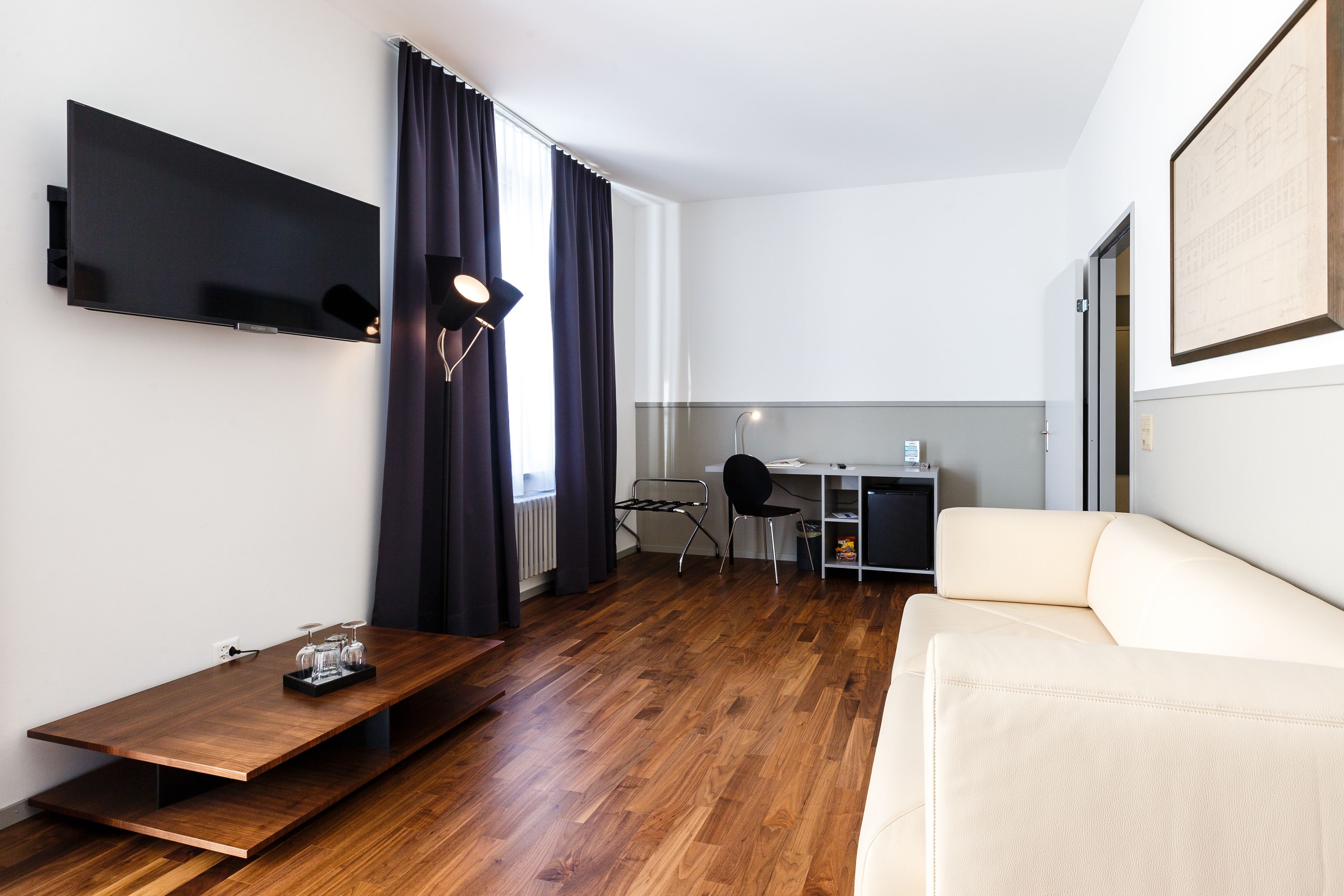 A modern living room with a flat-screen TV, a sofa, a coffee table, and a desk with a chair.