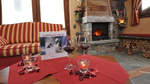 Um quarto aconchegante com lareira de pedra, um sofá vermelho e uma mesa posta com copos de vinho e velas.