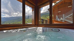 Uma banheira de hidromassagem com vista para uma paisagem montanhosa através de grandes janelas.