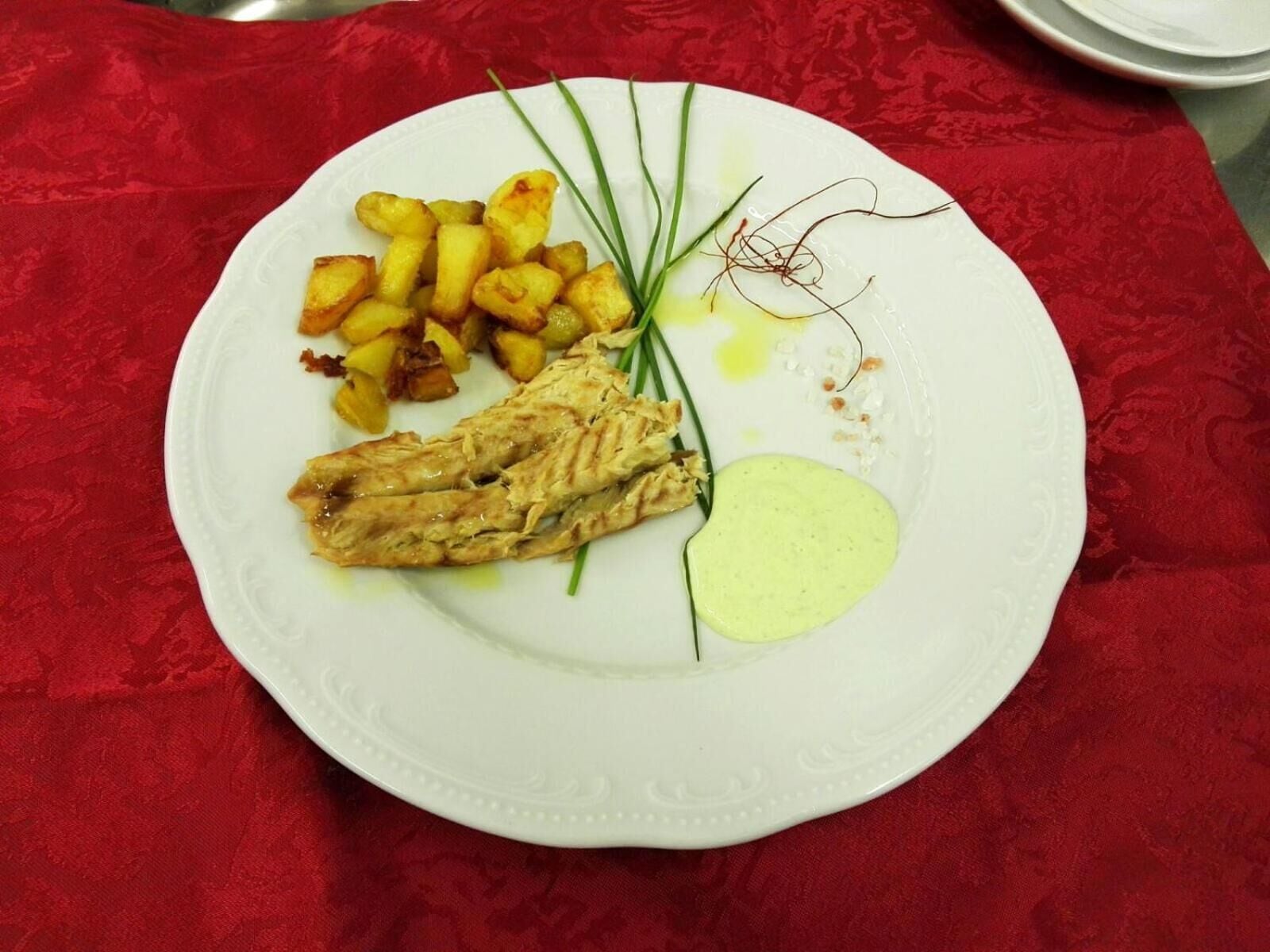 A plate with grilled chicken, roasted potatoes, and a green sauce on a white plate.