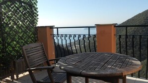 Una mesa redonda de madera y dos sillas en un balcón con baranda de metal, con vistas a un paisaje montañoso.