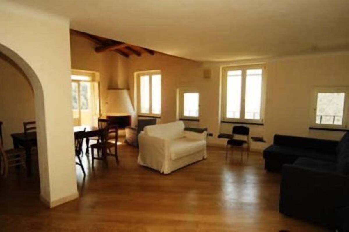 A spacious living area with wooden flooring, a white sofa, a black sofa, and a dining table with chairs.