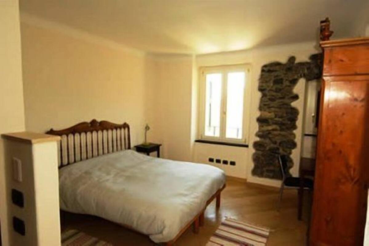 A bedroom with a bed, a nightstand, a dresser, a window, and a stone wall.