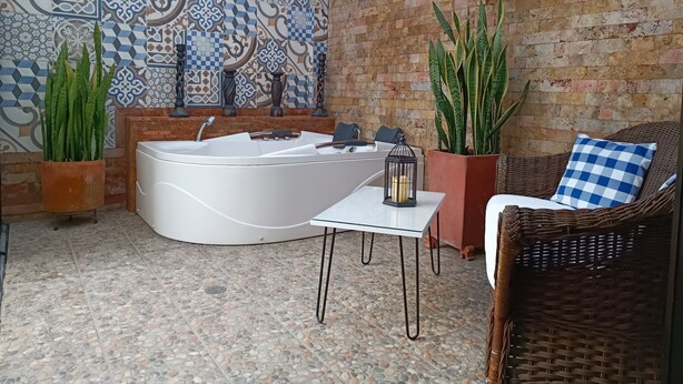 Zona de spa con una bañera grande, mobiliario de mimbre y azulejos decorativos.