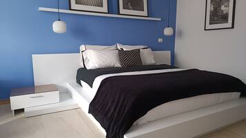 Un dormitorio moderno con una cama blanca, una mesita de noche y un aparador. Dos cuadros enmarcados decoran la pared sobre la cama.