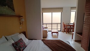 Habitación de hotel con cama, una mesita, una silla y balcón con vistas.