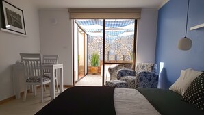 Un dormitorio con cama, escritorio y sillas, ventana con vista a un patio, y lámpara colgante.