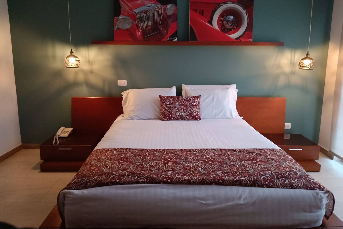 Une chambre d’hôtel avec un grand lit, deux tables de chevet, un téléphone et des œuvres d’art accrochées au mur.