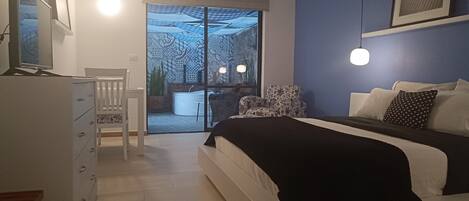 Un dormitorio con cama, escritorio, silla, cómoda y vista a un balcón con bañera.