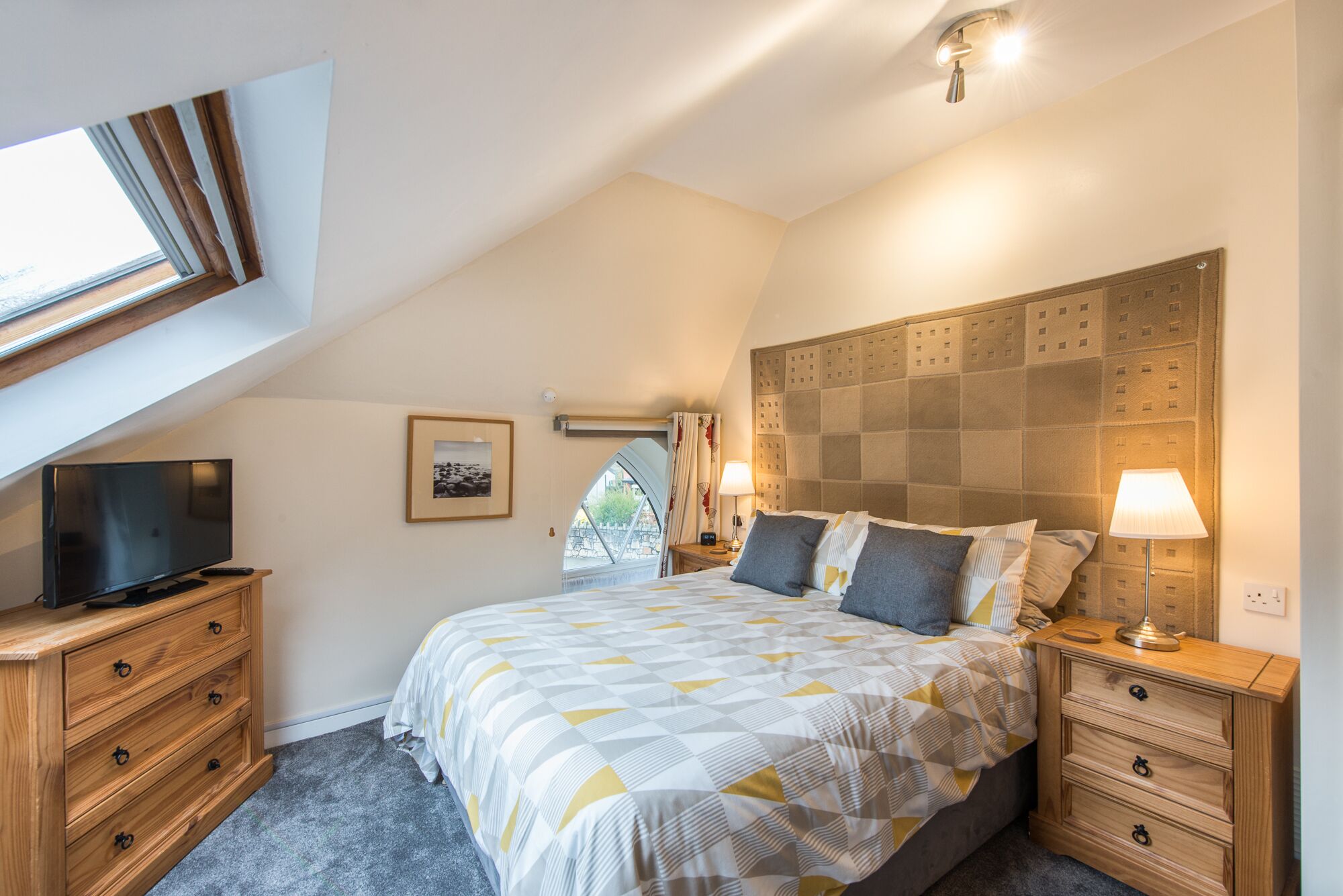 A bedroom with a large bed, wooden nightstands, a TV, and a window with a view.