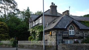 Un edificio de piedra con el letrero Tudor Lodge, que presenta fachada de piedra, un ventanal grande y una chimenea.