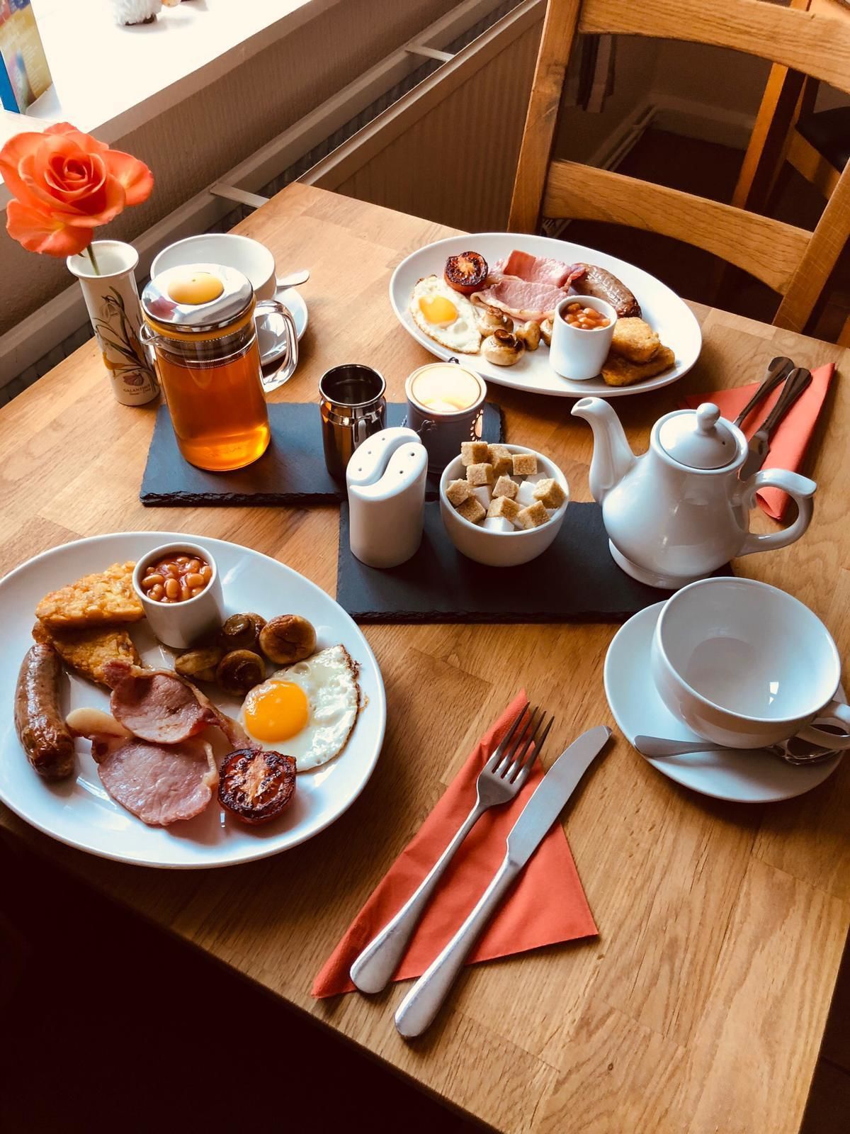 A breakfast setting with plates of eggs, sausages, and toast, a teapot, and a mug.