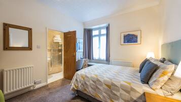 Une chambre à coucher avec un lit, un radiateur, une porte en bois, une fenêtre avec des rideaux et un tableau encadré au mur.
