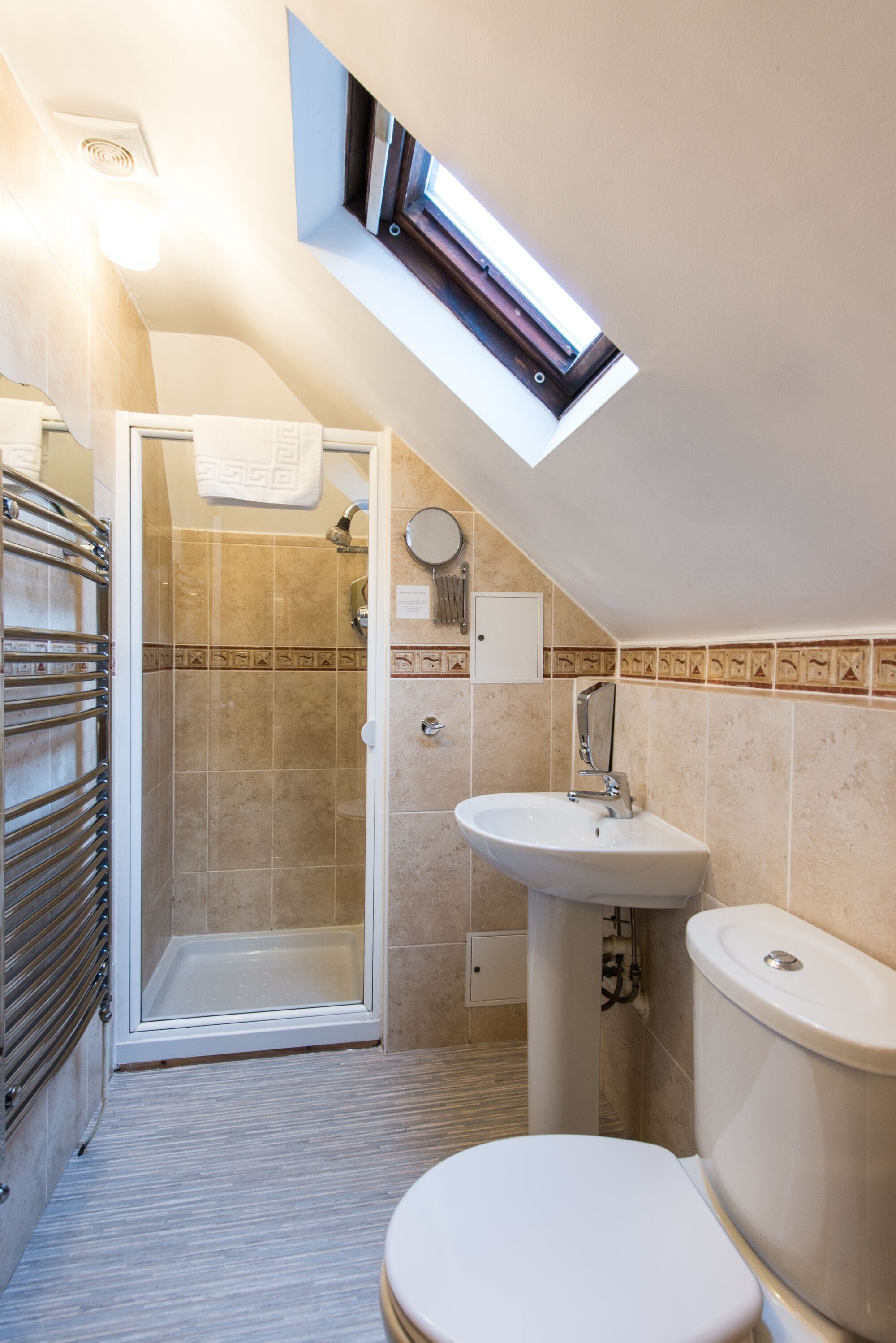Un baño con ducha, inodoro y lavamanos, que cuenta con un tragaluz y paredes con azulejos.