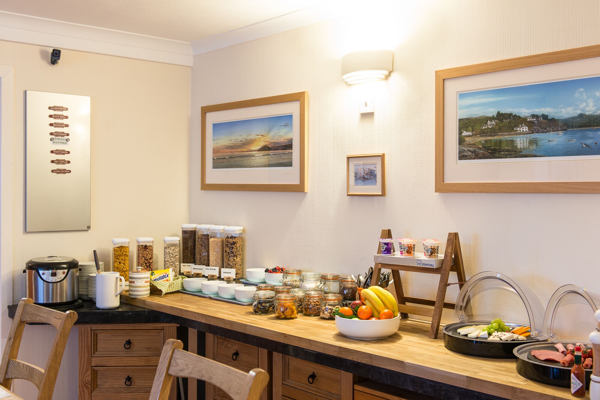 A breakfast buffet setup with various food items and condiments, a coffee machine, and a scenic view of a lake and mountains.