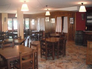A restaurant with wooden tables and chairs, hanging lamps, and a tiled floor. - El Jardín de la Huerta (Sahagun)