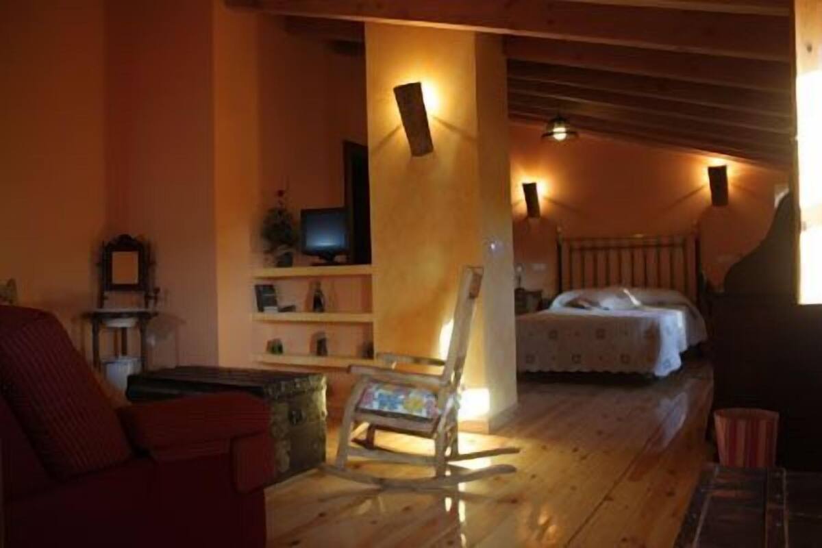 Een gezellige kamer met een houten vloer, een schommelstoel, een bed en een televisie op een plank.
