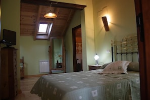 A bedroom with a bed, a nightstand, a lamp, a TV, a wooden ceiling, and a window. - El Jardín de la Huerta (Sahagun)