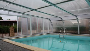 Ein überdachter Pool mit Glasveranda, einer Steinterrasse und Blick auf ein Gebäude im Hintergrund.