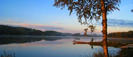 Um lago tranquilo com um píer que se estende pela água, rodeado por árvores e uma paisagem arborizada.