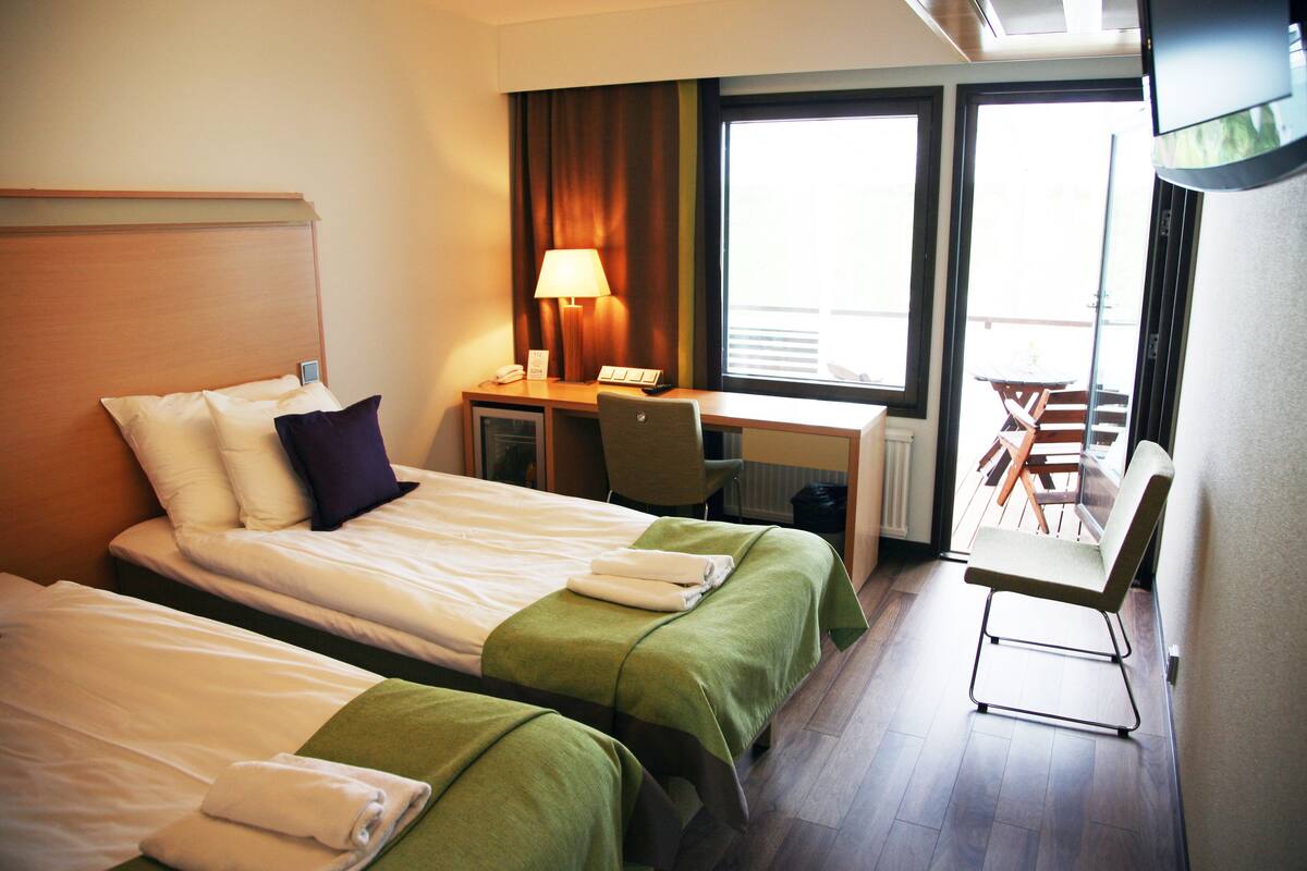 Habitación de hotel con dos camas, un escritorio, una silla y una ventana con vistas.